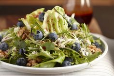 a salad with blueberries and walnuts in a white bowl on a striped tablecloth