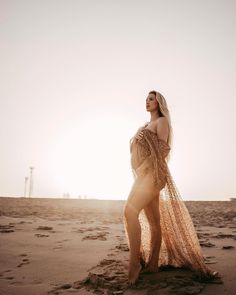 a woman standing on top of a sandy beach next to the ocean wearing a sheer dress