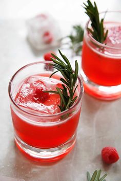 two glasses filled with red liquid and garnished with rosemary