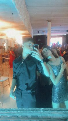 a man and woman taking a selfie in front of a mirror at a party