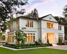 a large white house sitting on top of a lush green field next to a forest