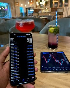 a person holding up a cell phone next to a drink on a table in a restaurant