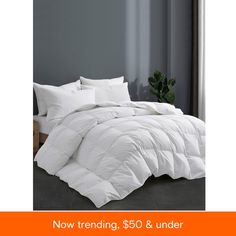 a white comforter on a bed next to a potted plant in a room