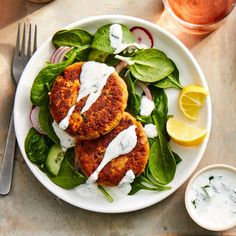 two crab cakes on a plate with spinach, cucumber and lemon wedges