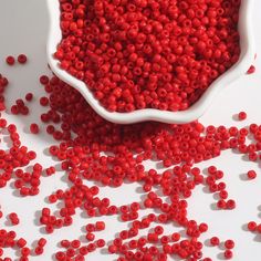 a white bowl filled with red beads next to a pile of smaller red bead sprinkles