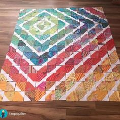 a multicolored patchwork quilt is laying on top of a wooden floor with wood floors