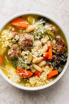 a white bowl filled with meatball soup and veggies on top of it