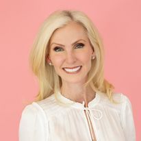 a woman with blonde hair and white blouse smiling at the camera while standing in front of a pink background