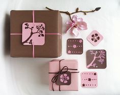 pink and brown gift boxes with tags on them sitting next to a tree branch decorated with flowers