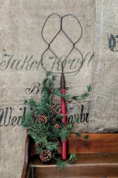 a christmas decoration with pine cones and red candles on an old wooden bench in front of a wall