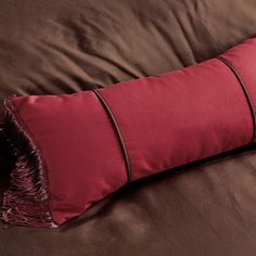 a brown and red pillow sitting on top of a bed next to a dark colored comforter