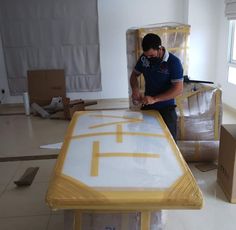 a man working on a table in a room with boxes around him and another person standing near the table