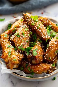 a bowl filled with chicken wings covered in sesame seeds and garnished with cilantro