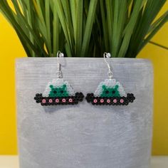 a pair of earrings with green and pink beads on them sitting next to a potted plant