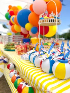 colorful balloons are hanging from the ceiling above a long table with striped cloths on it