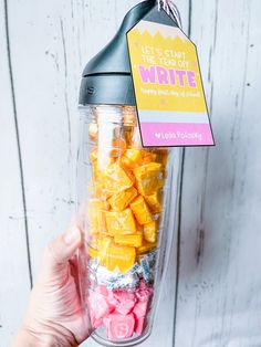 a person holding up a blender filled with gummy bears in front of a white wooden wall