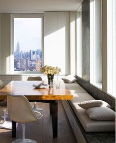 a dining room table with white chairs and a bench in front of a large window