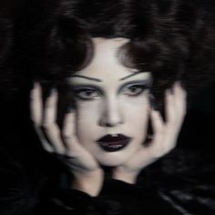 a woman with dark makeup and white make - up holding her hands to her face