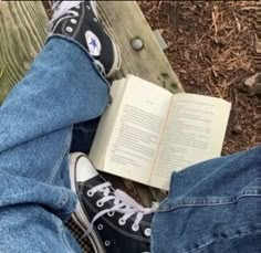 someone is reading a book while sitting on a bench with their legs crossed and wearing converse shoes