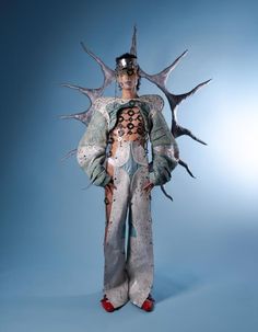 a woman in white and silver outfit with horns on her head, standing against a blue background