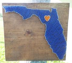 a string art map of the state of florida on a wooden board with a heart pinned to it