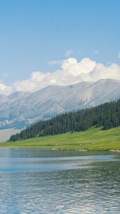 a lake with mountains in the background and grass on the bank, near to it