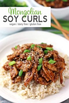 a white plate topped with rice covered in meat and green onions next to chopsticks