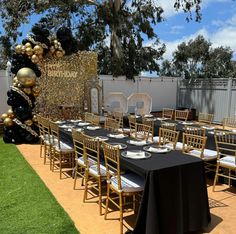 a table set up for a party with black and gold balloons on the back wall