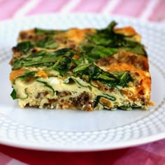 a white plate topped with a slice of quiche covered in cheese and spinach