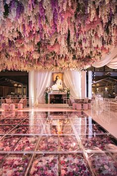 an indoor wedding venue with pink and white flowers hanging from the ceiling, surrounded by clear acrylic flooring