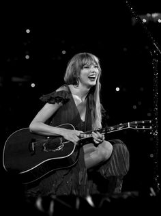 a woman sitting on top of a stage holding a guitar and singing into a microphone