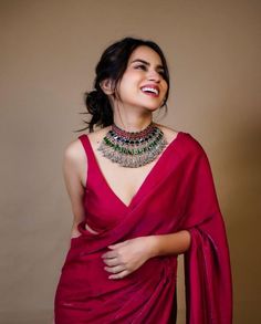 a woman in a red dress with a necklace on her neck, smiling and looking up at the camera