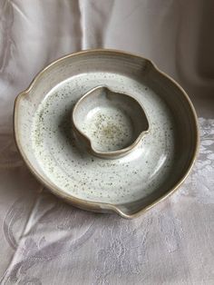 a white bowl sitting on top of a table next to a cloth covered bed sheet