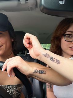 two women sitting in a car with tattoos on their arms