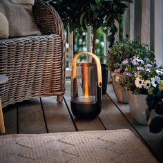 a small lantern sitting on top of a wooden floor next to potted plants and a wicker chair