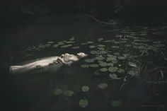 a woman is floating in the water with lily pads on her back and head down