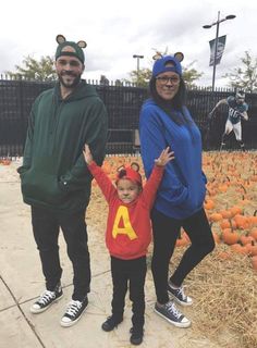 two adults and a child standing in front of pumpkins