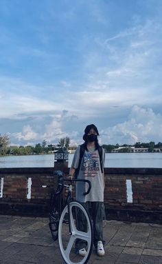 a person standing next to a bike on a brick walkway near the water with a sky background