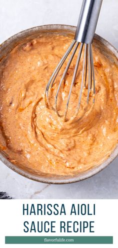 a bowl filled with sauce next to a whisk on top of a table