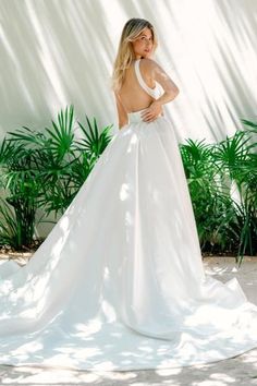 a woman in a white wedding dress posing for the camera with palm trees behind her