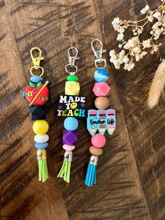 three different key chains on top of a wooden table next to some flowers and a feather