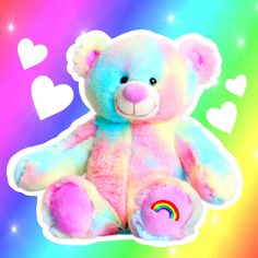 a rainbow colored teddy bear sitting in front of a colorful background with hearts on it