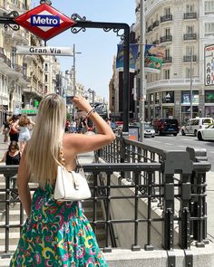 a woman in a colorful dress is looking at the metro sign above her head on a city street