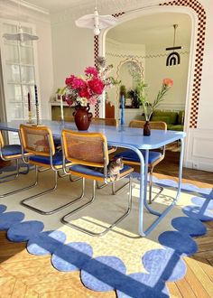 a blue table with four chairs in front of it and flowers on the floor next to it