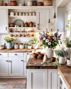 a kitchen filled with lots of white cupboards and wooden counter tops covered in pots and pans