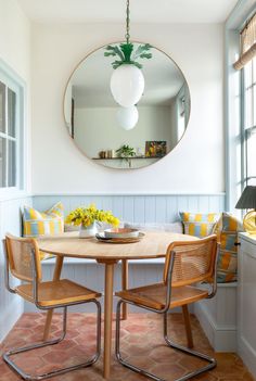 a round mirror hangs above a wooden table with chairs and yellow flowers on the table