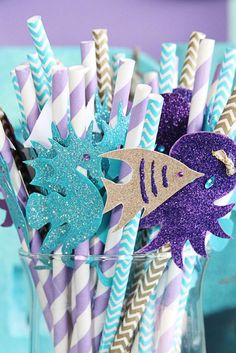 purple and blue paper straws with fish on them in a glass vase filled with water