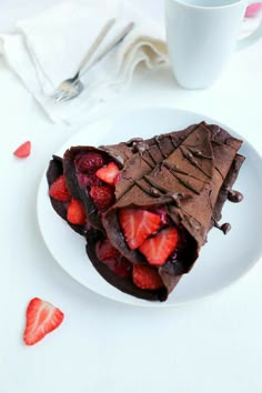 a white plate topped with chocolate and strawberries next to a cup of coffee on top of a table