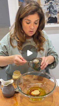 a woman is pouring oil into a glass bowl on top of a wooden table with other items