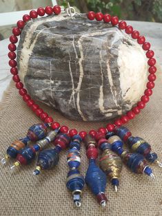 a red beaded necklace and several other beads sitting on a table next to a rock